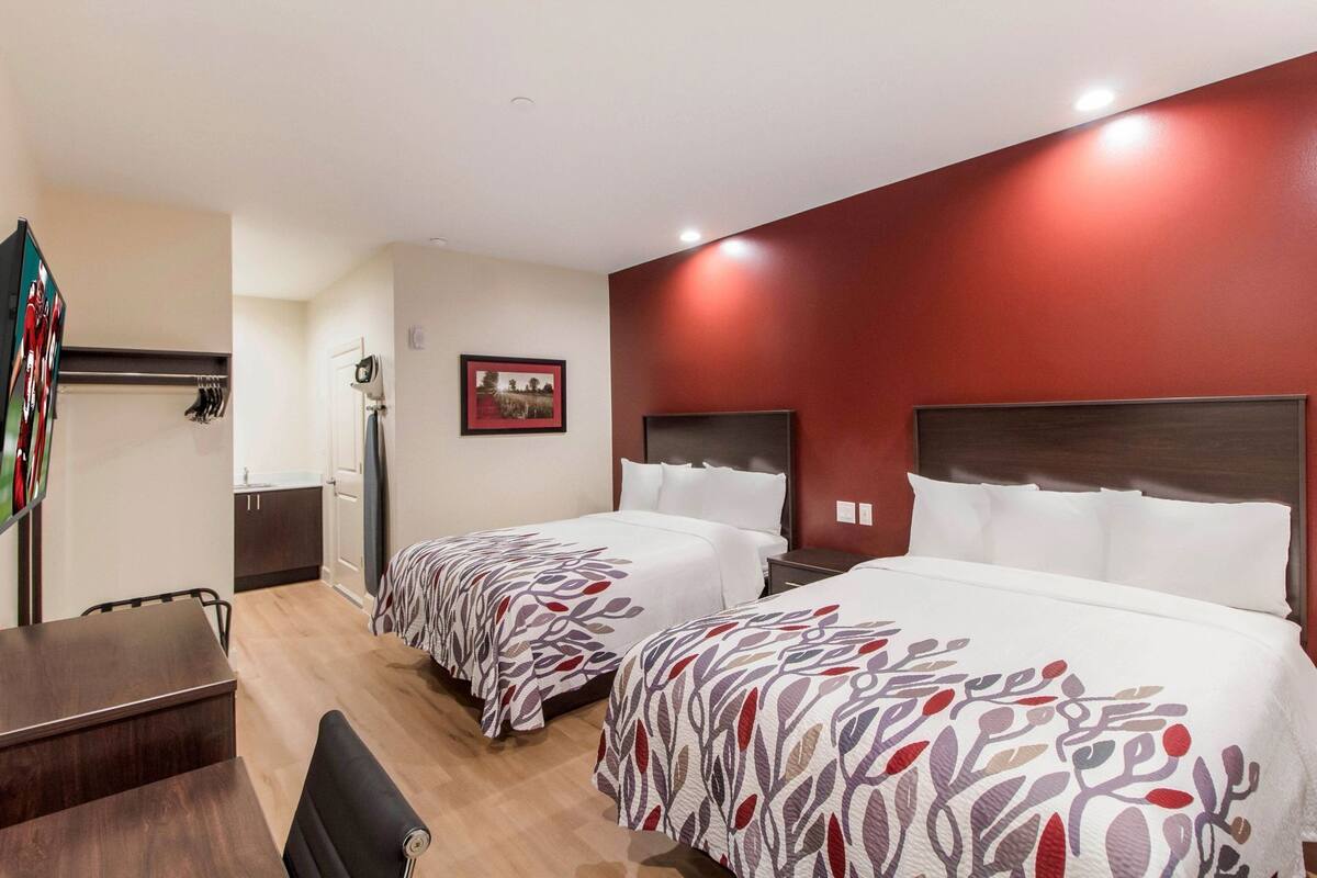 A hotel room with two beds, a desk, a chair, a TV, and a picture on the wall.