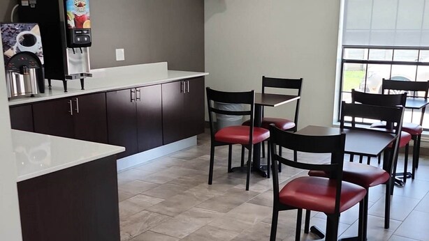 A modern kitchen with dark cabinets, a white countertop, and a dining area with red chairs and a table. - Red Roof Inn Houston - Willowbrook (Houston)