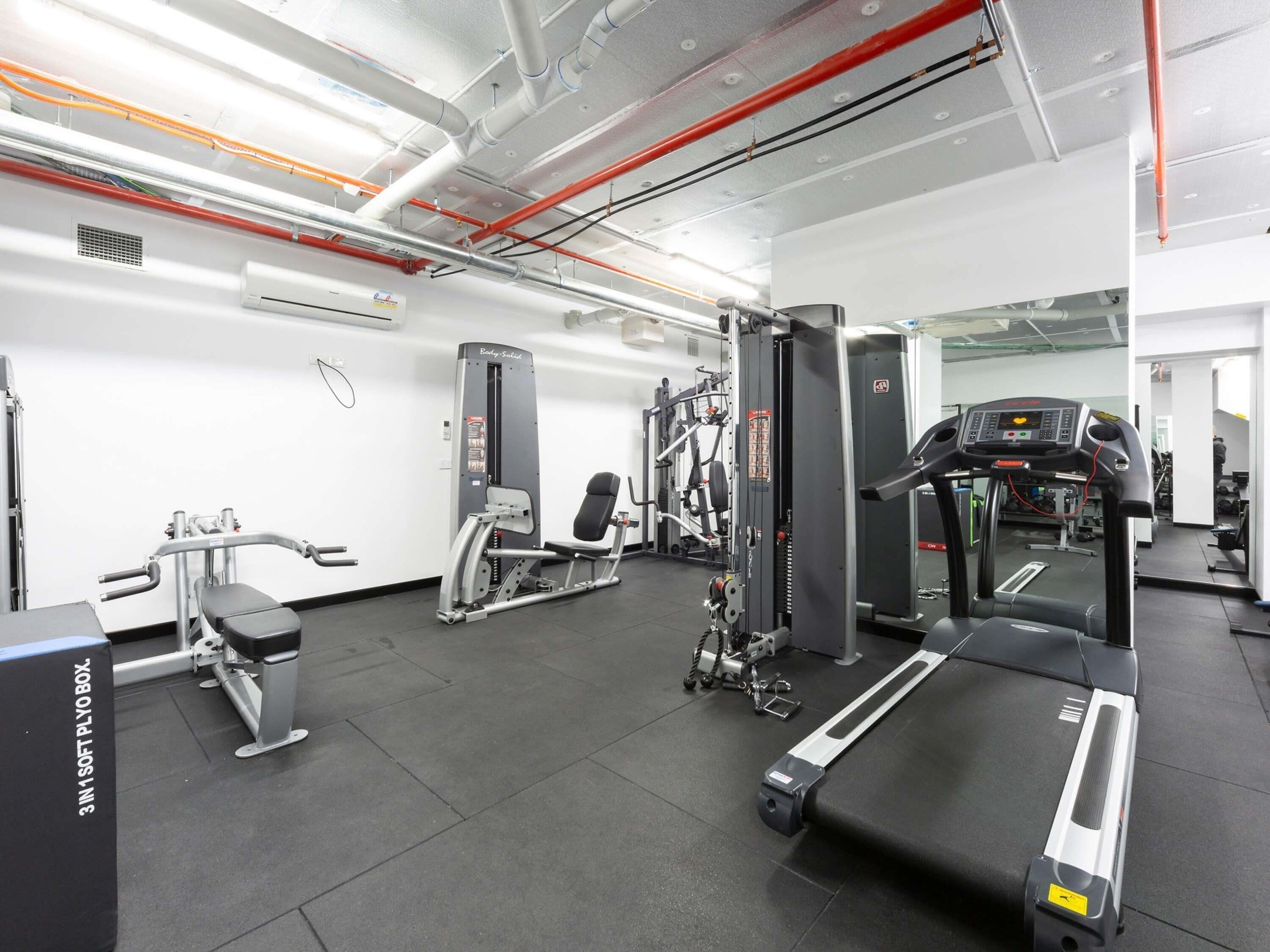 Une salle de sport équipée de divers appareils d’exercice, notamment un tapis de course, des appareils de musculation et un banc de développé couché.