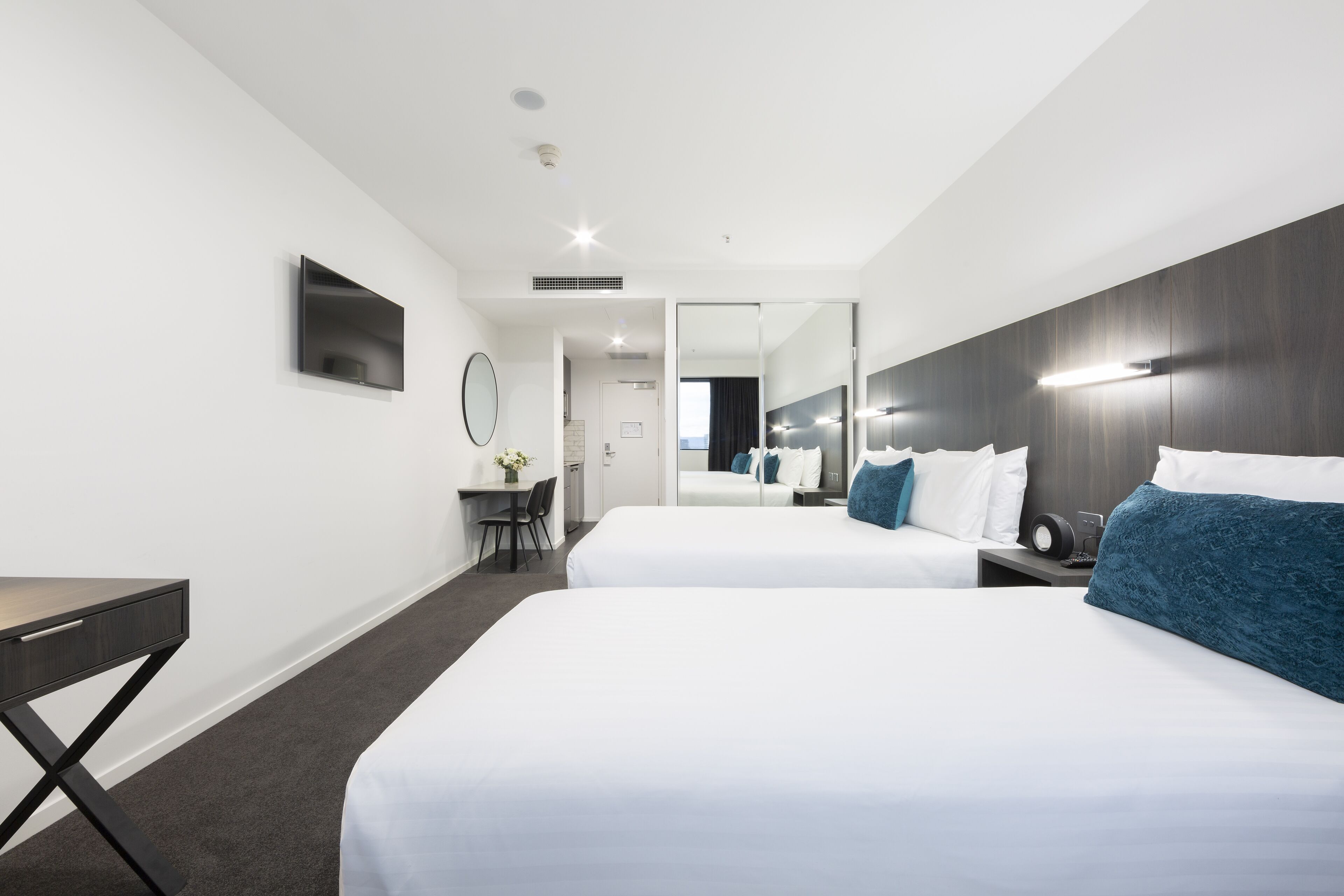 Una habitación de hotel moderna con dos camas, un escritorio y un espejo.