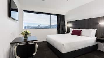 Une chambre d’hôtel équipée d’un lit, d’un bureau, d’une chaise et d’une grande fenêtre donnant sur la ville.