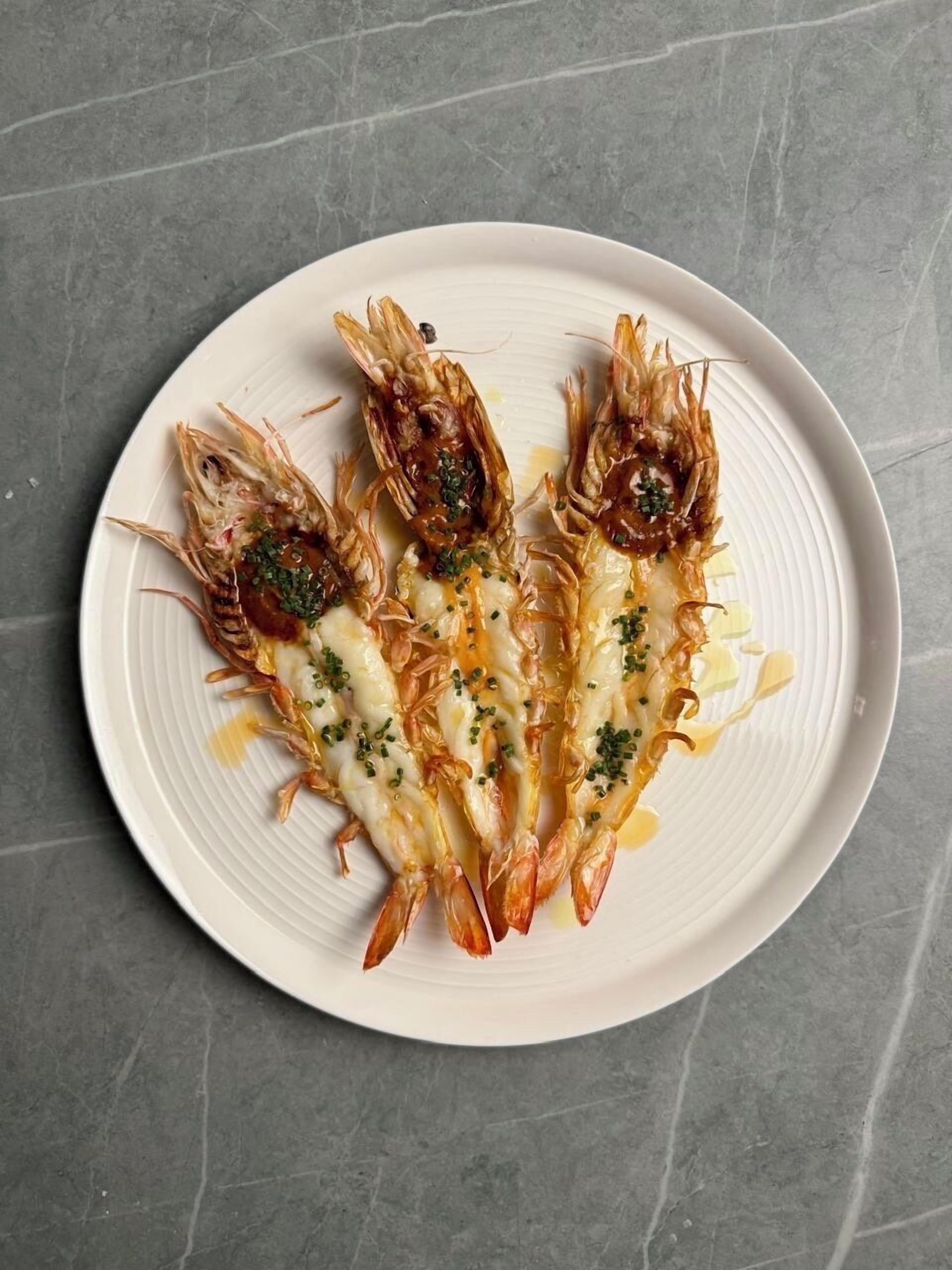 Un piatto di gamberi cotti con salsa cremosa e guarnizione verde, su un piatto bianco.