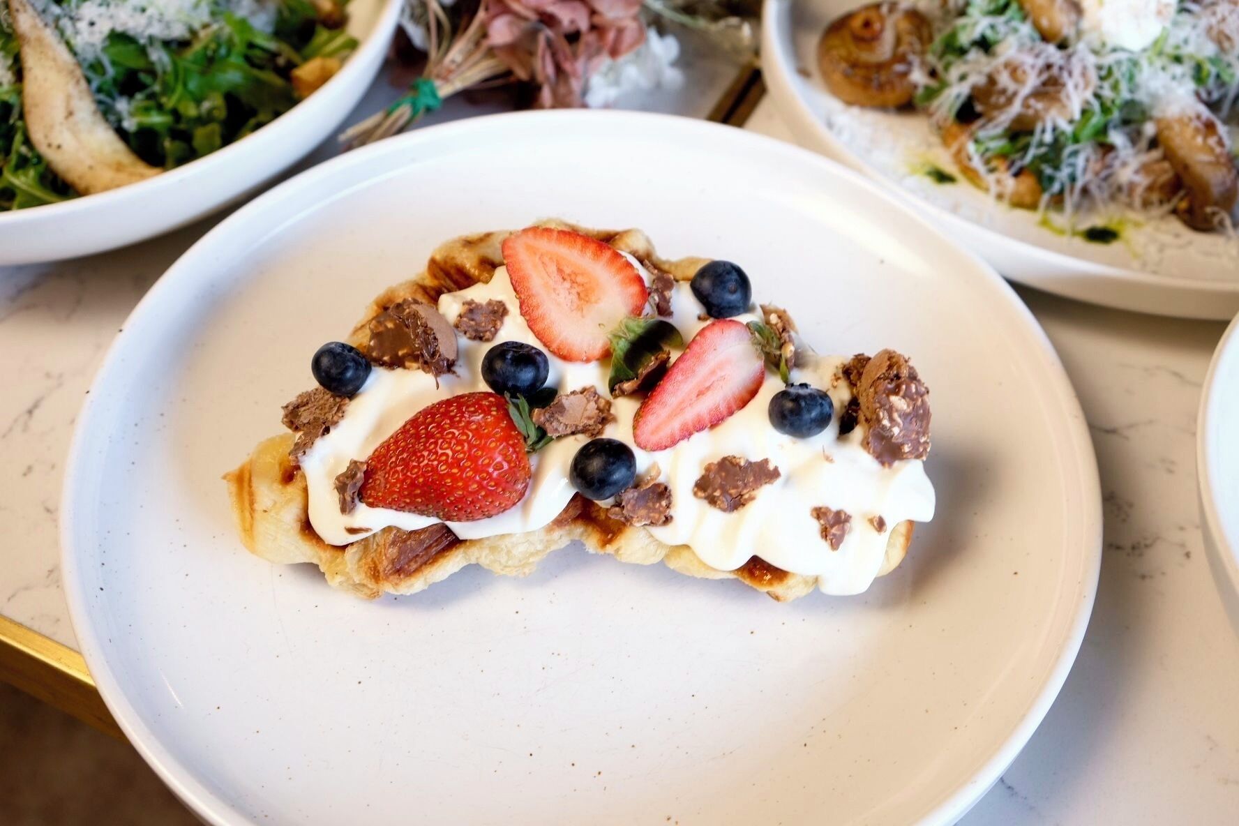 A dessert plate with a pastry topped with strawberries, blueberries, and chocolate pieces.