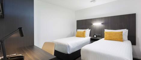 A hotel room with two beds, a desk, a chair, and a lamp.