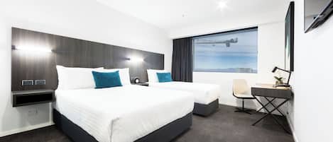 Habitación de hotel con dos camas, un escritorio, una silla, un amplio ventanal con vista panorámica de la ciudad y un televisor de pantalla plana montado en la pared.