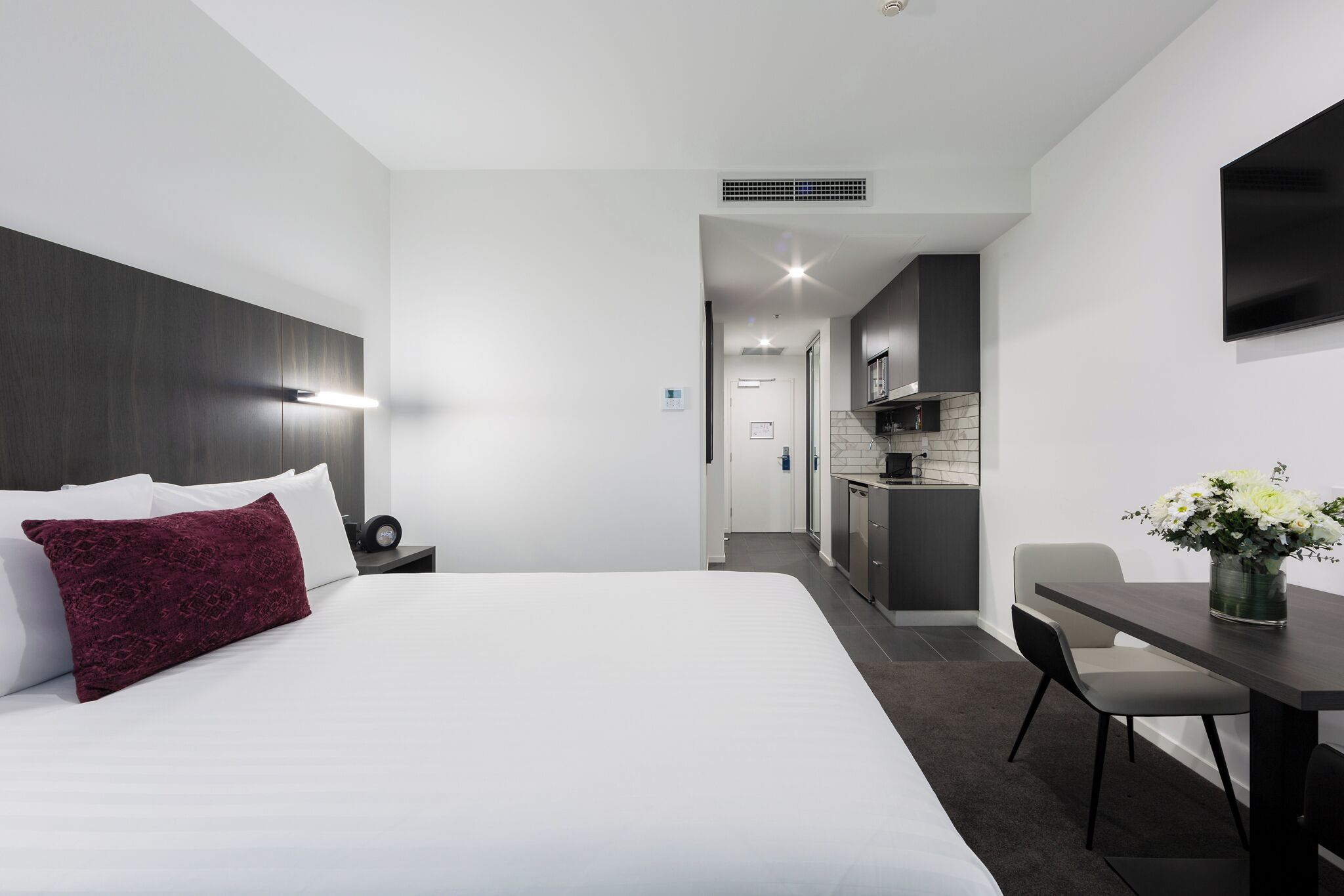 Une chambre d’hôtel moderne avec un grand lit, un bureau et, au fond, une petite cuisine.