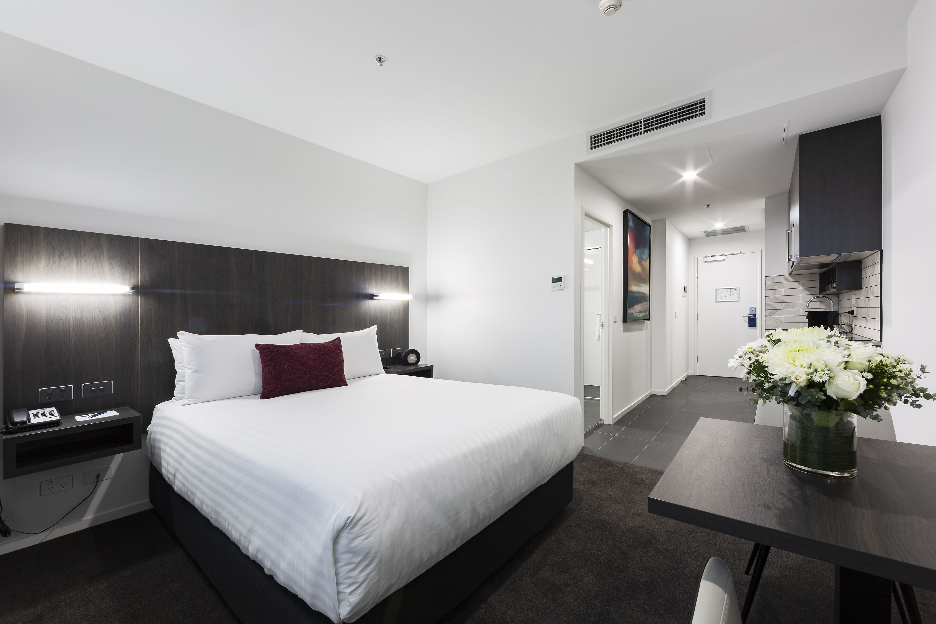 Quarto de hotel moderno com uma cama grande, mesas de cabeceira, escrivaninha e uma cadeira.
