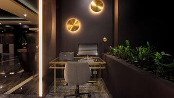 Um espaço de escritório moderno com uma mesa de vidro, um computador e uma cadeira. Há duas luminárias circulares fixadas na parede e uma planta à direita.