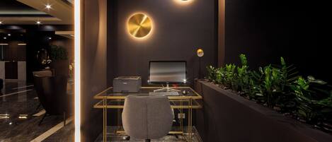 Un espacio de oficina moderno con un escritorio de vidrio, una computadora y una silla. Hay dos lámparas circulares fijadas a la pared y una planta a la derecha.