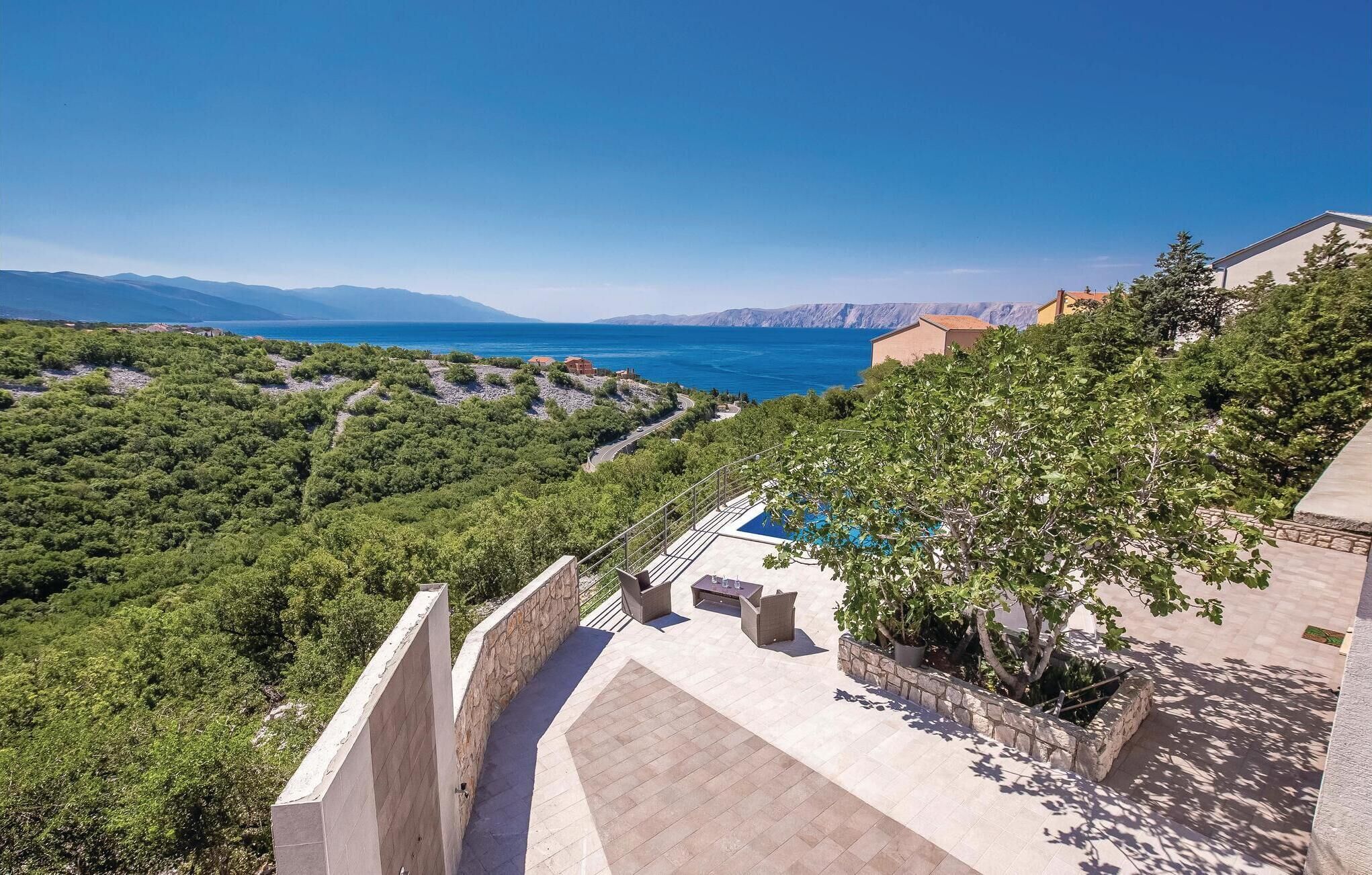 A terrace with outdoor furniture overlooking a mountainous landscape and the sea.
