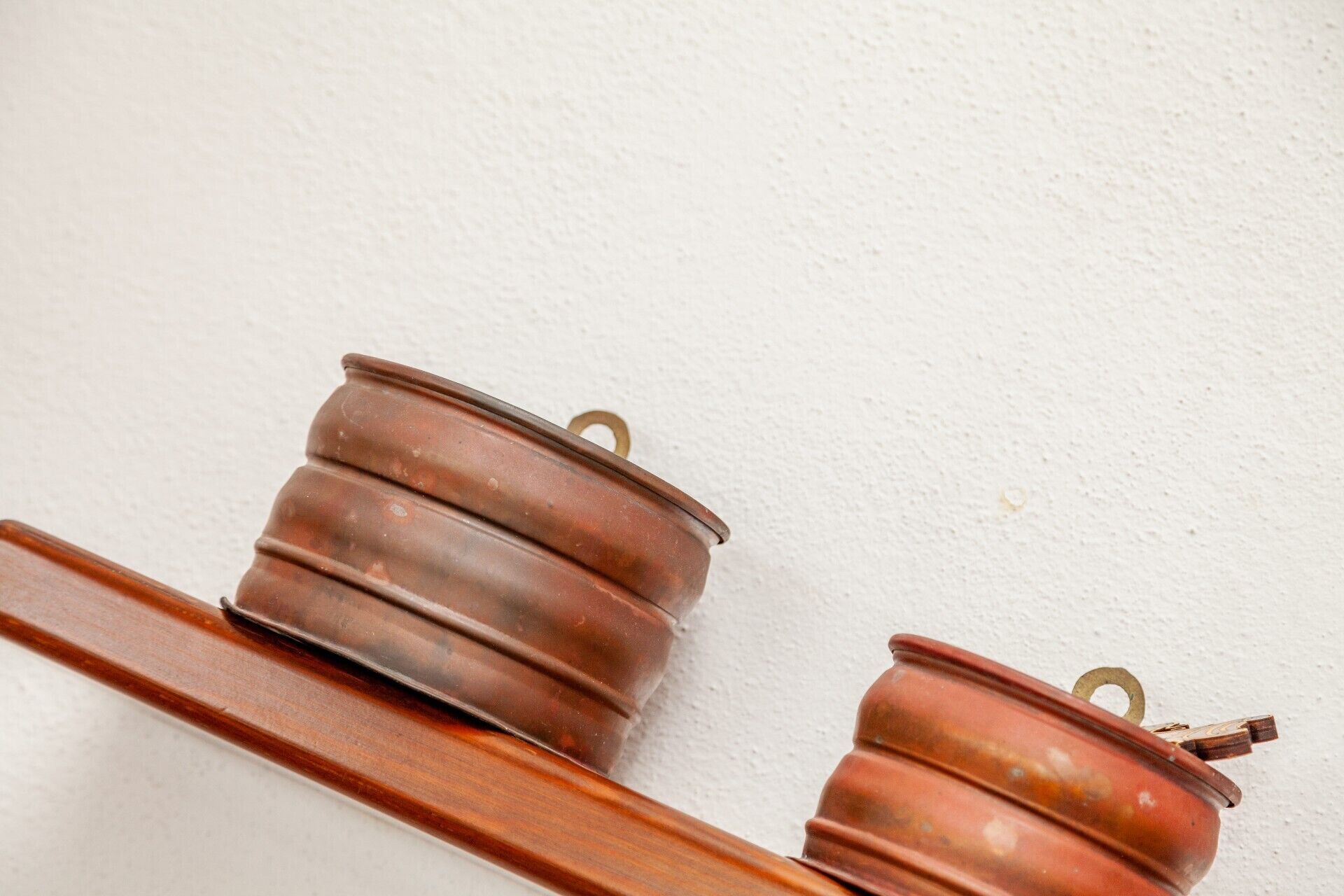 Dos contenedores metálicos cobrizos con asas, probablemente para guardar objetos, sobre una estantería de madera frente a una pared blanca.