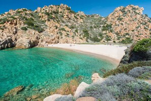 Una spiaggia costiera con acque turchesi cristalline, scogliere rocciose e una riva sabbiosa.