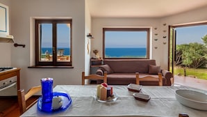 Una sala de estar acogedora con un amplio ventanal que ofrece vistas al mar, una mesa de comedor con velas y un sofá.