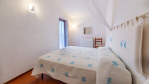Un dormitorio con cama, mesita de noche, cómoda, espejo y ventana con cortinas.