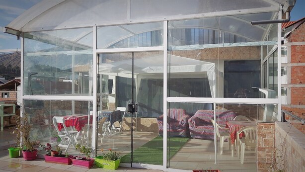 Un invernadero con paredes de vidrio, un patio con sillas y una mesa, y plantas en macetas.