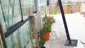 Un balcón con macetas dispuestas en fila, una ventana con vista a la ciudad y un suelo de baldosas.