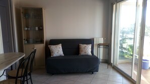 Un espace de vie compact avec un canapé foncé, deux coussins à motifs, une petite table et un meuble vitré.