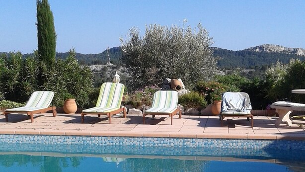 Une piscine dont les bords sont recouverts de carreaux, entourée de chaises longues et de plantes en pot.