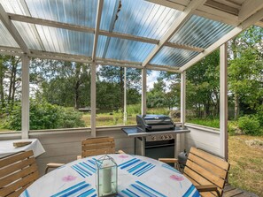 Une terrasse extérieure couverte, équipée d’un barbecue, de meubles en bois et offrant une vue sur un paysage naturel.
