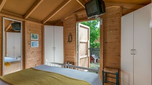 Un dormitorio de cabaña de madera con una cama, un televisor y una ventana con vistas a un jardín.
