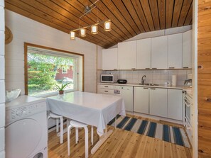 A compact kitchen with a wooden ceiling, white cabinets, a microwave, a sink, and a table with chairs. - Lampaluodon punainen tupa by Interhome (Pori)