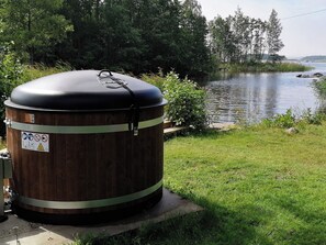 A large cylindrical water tank with a lid, situated on a concrete base near a body of water and greenery.