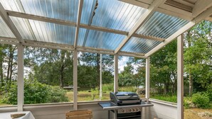 Un espacio al aire libre techado con una parrilla, una mesa con sillas y vistas a un paisaje natural.