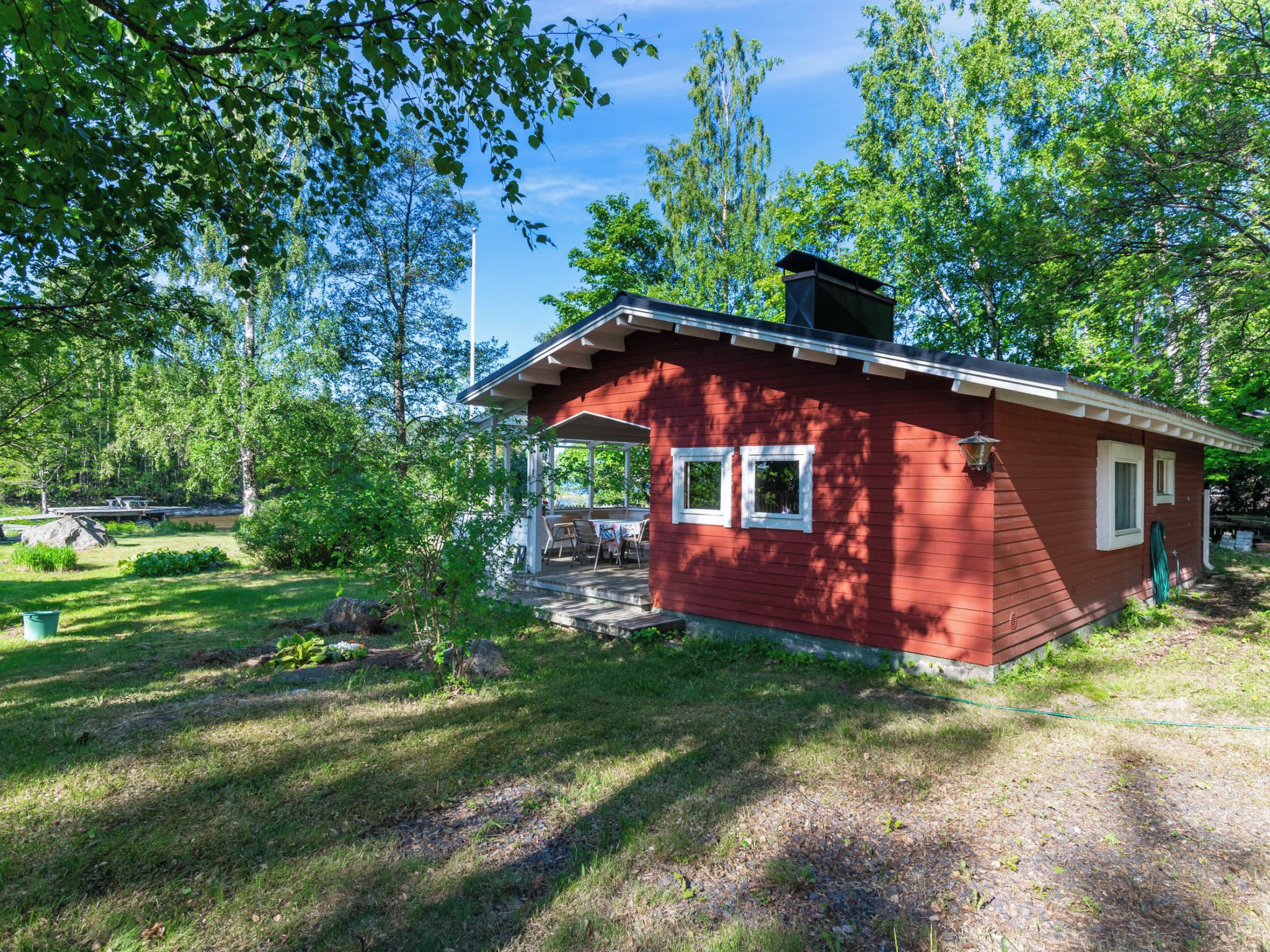 Een kleine rode hut met een veranda, omgeven door bomen en een gazon.