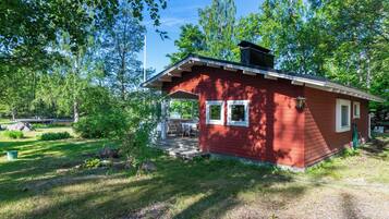 Een kleine rode hut met een veranda, omgeven door bomen en een gazon.