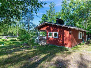 A small red cabin with a porch, surrounded by trees and a grassy yard.