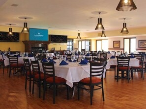 A restaurant with multiple tables set for dining, featuring a blue sign with white text, wooden chairs, and hanging pendant lights.