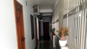 A corridor with a polished stone floor, a wooden door on the left, and a metal railing on the right.