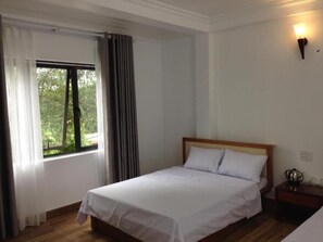 A bedroom with a single bed, a nightstand, a wall-mounted lamp, and a window with curtains. - Hanh Hoa Hotel (Hai Phong)
