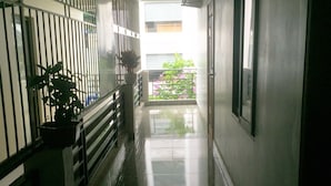 A corridor with a metal railing on one side, a potted plant, and a view of a balcony with flowers.