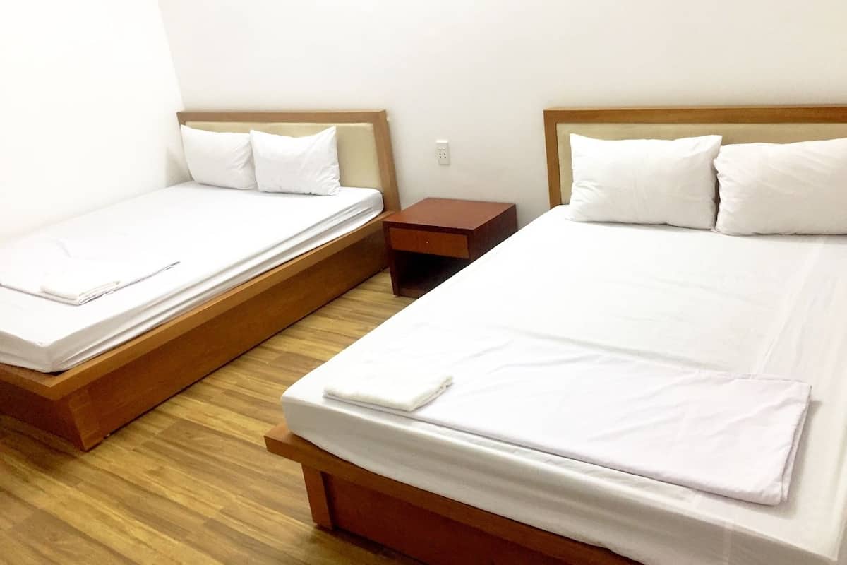 A hotel room with two single beds, wooden headboards, white bedding, and a small wooden nightstand.