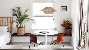 Une cuisine moderne avec un plan de travail foncé, deux chaises en bois, une table ronde blanche et un luminaire suspendu en fibres tressées.