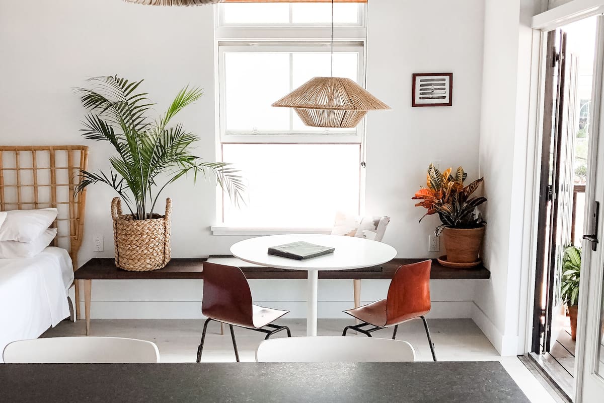 A modern kitchen with a dark countertop, two wooden chairs, a round white table, and a hanging woven light fixture.