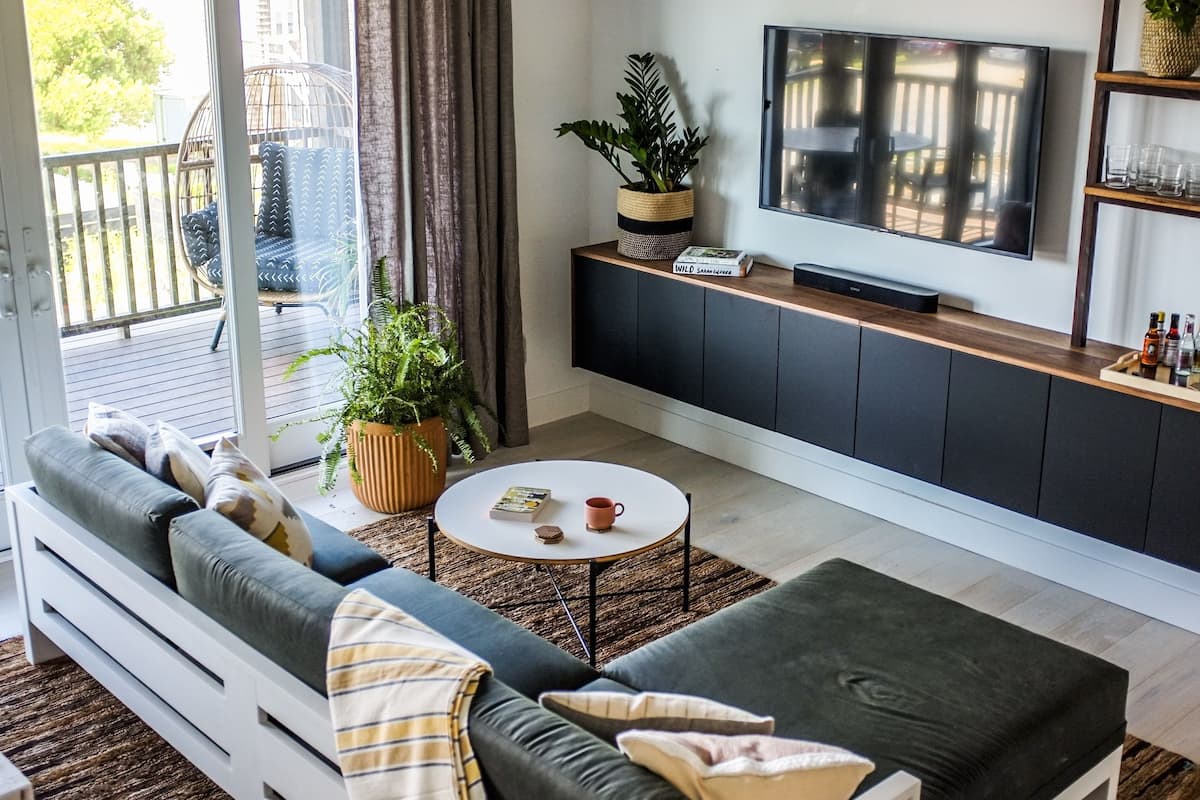A modern living room with a sofa, ottoman, coffee table, and a TV on a wall.
