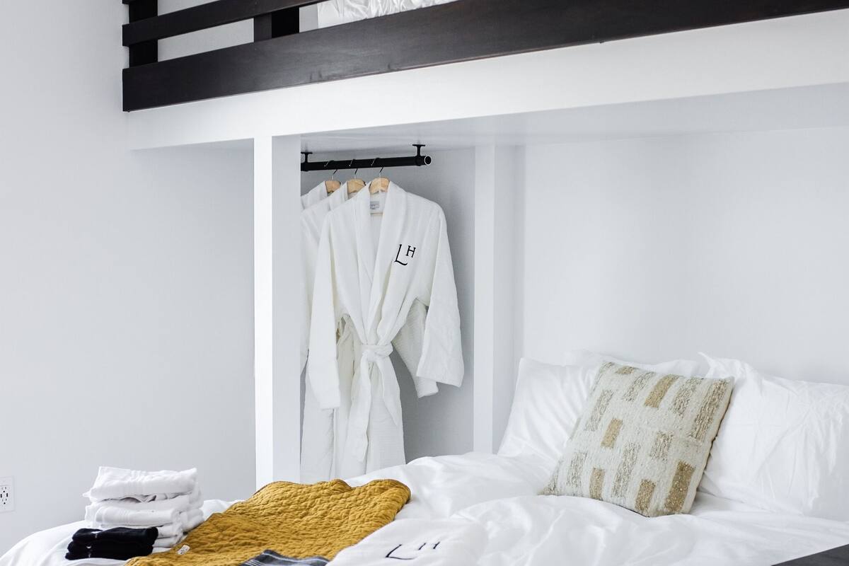 A modern bedroom with a bunk bed, a bedside table, a wardrobe, and a bed with neatly folded towels and a blanket.