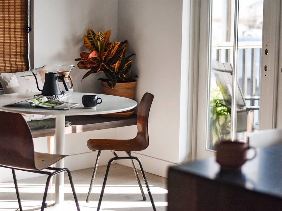Un comedor moderno con una mesa redonda, dos sillas, una cafetera, una planta en maceta y un ventanal con vistas a zonas verdes.