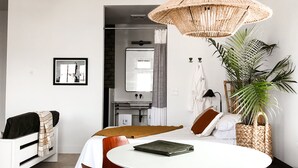 Une pièce moderne et bien éclairée, avec une table de salle à manger ronde, des chaises marron, un luminaire suspendu en fibres tressées et une plante en pot.