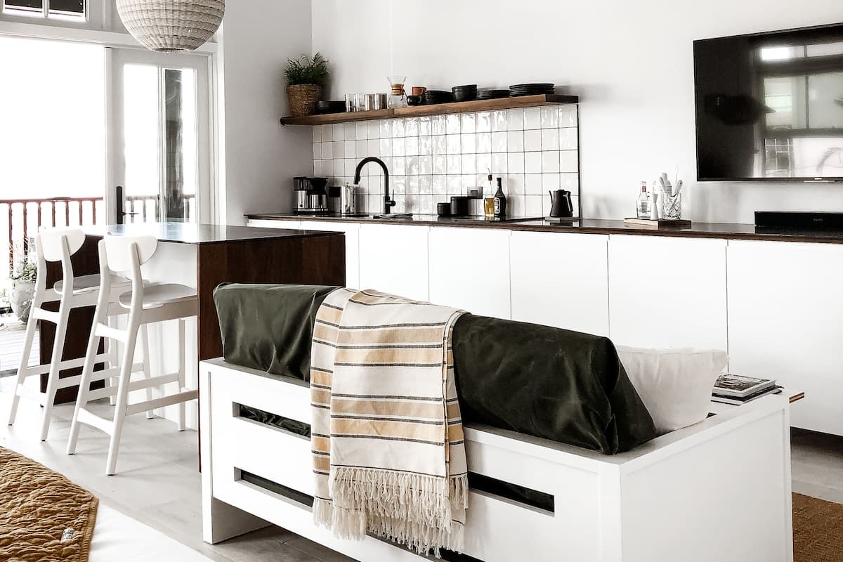 A modern kitchen with white cabinetry, a hanging light fixture, and a built-in TV.