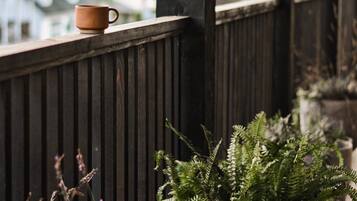 A wooden balcony with a rustic fence, a potted fern, and a cup on the railing.