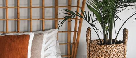 A bed with a white comforter and a brown throw blanket, a woven plant pot on a bedside table, and a bamboo headboard.