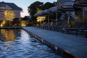 Een zwembadgedeelte met ligbedden en parasols, een bordje met 'Local Hotel' en een reflectie in het water.