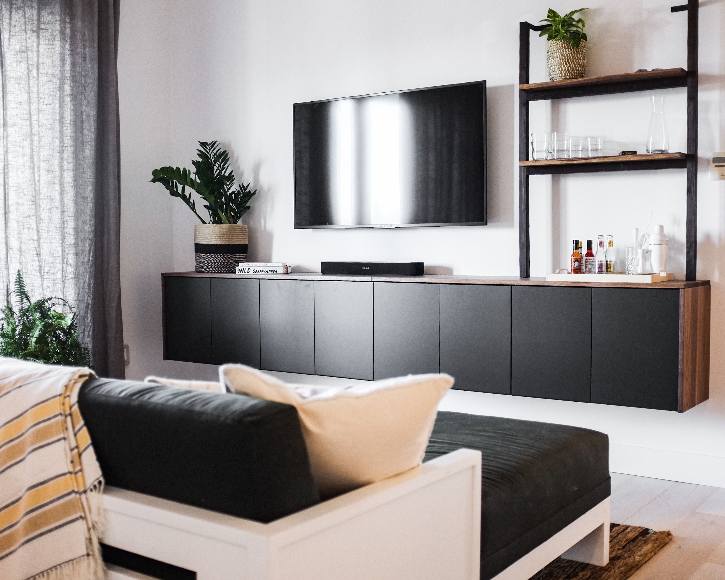 Un salon moderne avec un téléviseur à écran plat fixé au mur, un meuble en bois foncé en dessous, et un canapé blanc agrémenté de coussins à rayures.