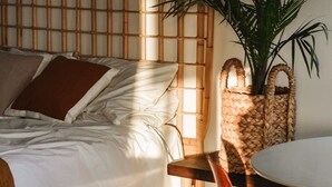 Une chambre à coucher avec un lit, une tête de lit en bois, un panier en osier, une chaise et une plante en pot.
