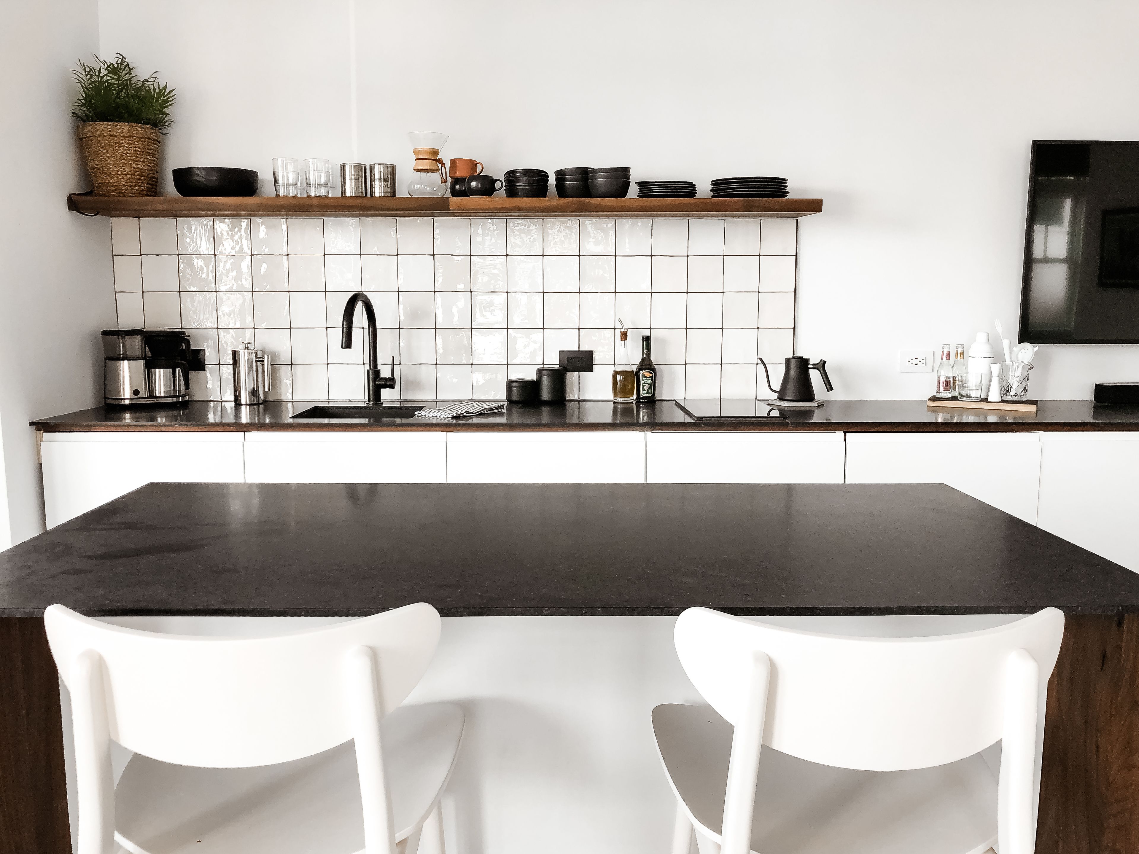 A modern kitchen with a central island, white chairs, and a variety of kitchenware on the countertop.