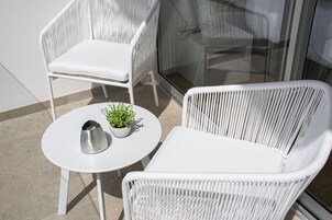 Un conjunto de silla y mesa de mimbre blanco en un balcón con una puerta de vidrio y una pequeña planta en maceta.