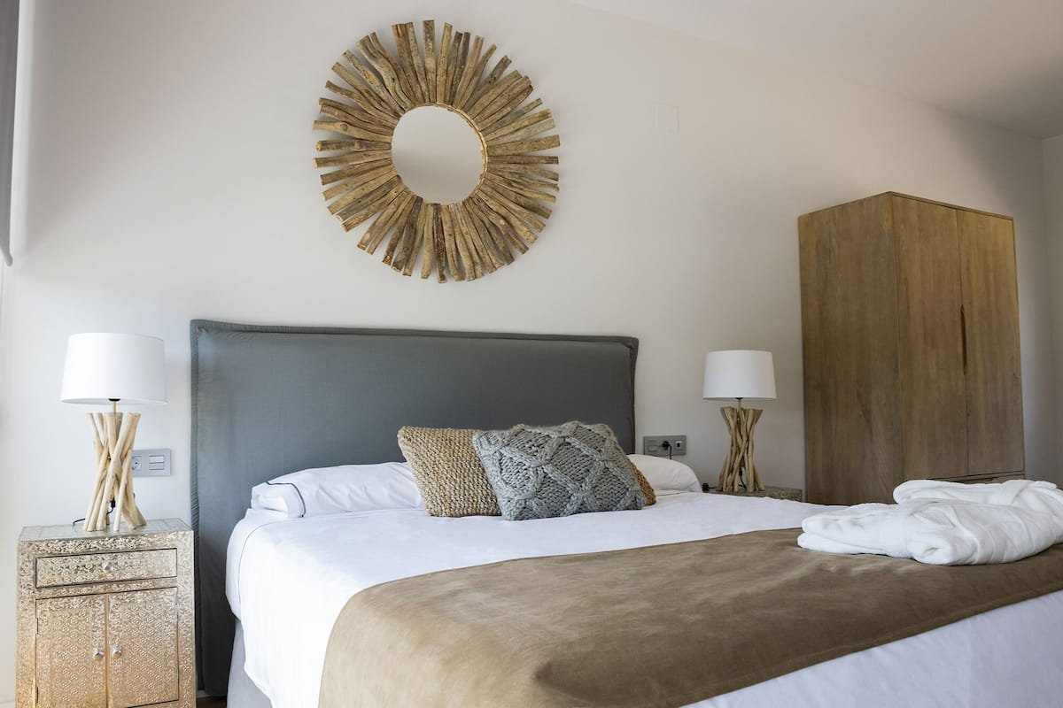 A neatly made bed with a grey headboard, two bedside lamps, and a large wooden wardrobe.